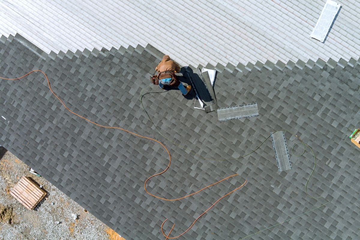 A asphalt shingles installation on the roof roofer is nailing asphalt shingles to a roof in Woodbury