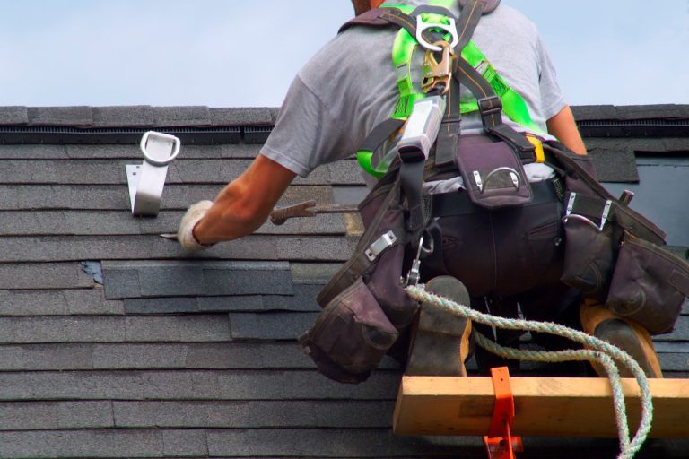 Roofer repairing asphalt shingles on a roof of a Woodbury house